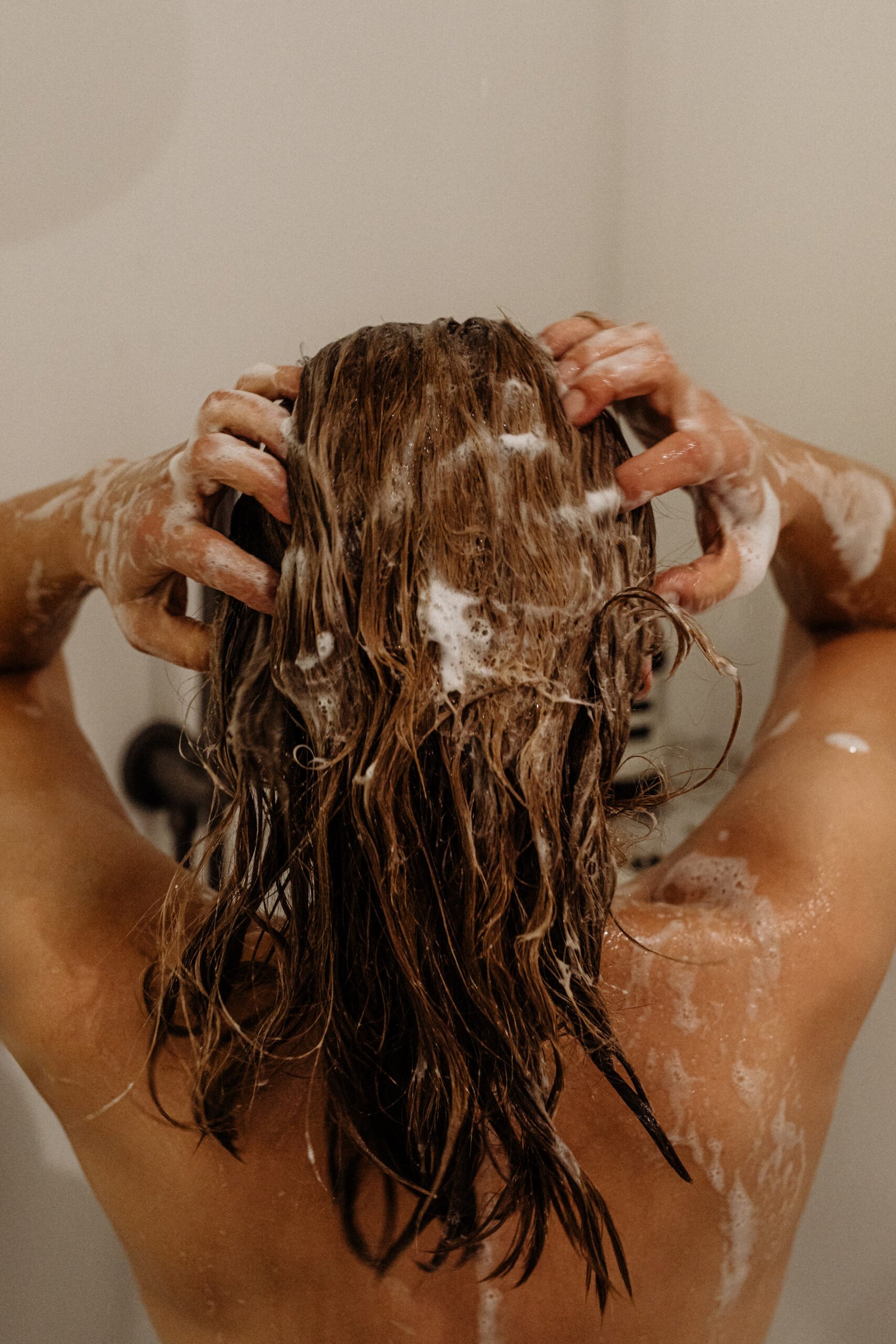 Lifestyle image of woman shampooing hair in shower with bask to us